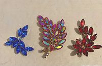 Front view of three vintage rhinestone pins: large one with multicolored stones signed Webb, and two smaller in blue and red rhinestones.