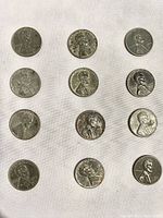 Top view of the obverse of 12 vintage 1943 steel pennies on a white background showing Abraham Lincoln's profile with surface wear and discoloration.