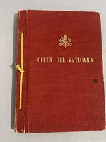 Front cover of the stamp album, reddish fabric cover with papal insignia and 'Città del Vaticano' text in gold emboss.