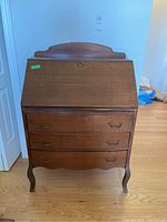 Front view of the closed bureau desk showing the wood finish, three drawers with drop handles, and the upper hinged writing surface in closed position.