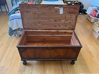 Front angled view of the vintage wooden blanket box with hinged lid open showing lighter wood interior and carved scroll designs on dark wood exterior.