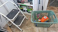 Wide shot showing white two-step stool, green laundry hamper, floor tiles and cleaning supplies on lower shelves.