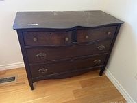 Front view of vintage wooden dresser with four drawers, showing overall condition and curved design separating drawers