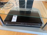 Front view of black Toshiba combo unit with glass flip-up lid on top and media slots front center and right side.