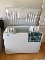 Front view of the chest freezer with lid open, showing two removable plastic baskets inside and a green checkered cloth on the side.