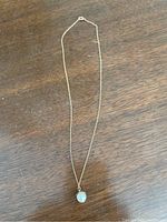Full length of the gold chain with pearl pendant lying flat on a wooden surface.