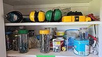 Shelf with Makita drill, ear guards, jars and containers of nails, screws and other household hardware items.