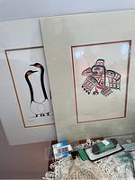 Two framed prints by Bill Reid showing stylized bird and winter scenes, partially overlapping with some lace and sewing supplies visible.