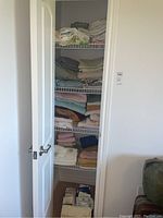 Closet shelves filled with stack of folded linens including sheets, towels, and cloths