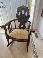 Front facing view showing the engraved detailed backrest, curved arms, and cushioned seat with some staining.