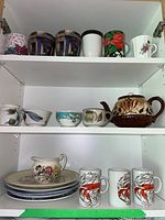 Full shelf view showing 3 lobster mugs, 6 pottery mugs, 5 plates, and ceramic teapot.