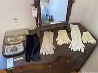 Five pairs of vintage gloves and two purses on a wooden dresser with mirror.