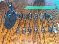 Photo showing seven silver-tone Rolex Bucherer spoons with embossed lion and crown designs laid out on a wooden surface alongside a metal crumb tray.
