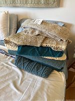 Stack of various knit sweaters folded on bed showing colors and textures