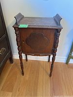 Front view of vintage wooden end table showing raised quatrefoil-shaped detail on cabinet door and tapered spindle legs.