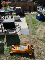 Yellow 2 1/4 ton capacity hydraulic garage jack with a long white handle standing upright on grass with outdoor background.