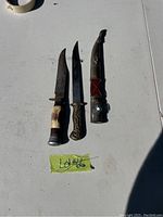 Two daggers and one sheath arranged on a table with lot number visible.