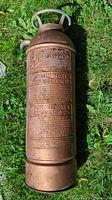 Full length front view showing embossed instructions and branding on copper/brass extinguisher body.