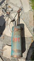 Full view of copper fire extinguisher with hose and handle on stone floor.