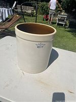 Full view of antique 4 gallon crock showing cream exterior and brown glazed interior sitting on table outdoors.