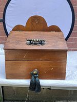 Front view of antique wooden storage box showing hinged top compartment with brass handle and lower drawer with tassel pull.