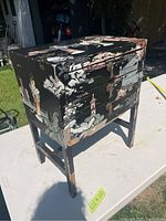Side view of the Asian-style side table showing painted black finish with beige and brown decorative artwork, and visible chipping on legs and sides.