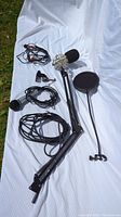 Full kit laid out on white fabric showing microphone with shock mount and foam cover, arm stand, pop filter, and cables