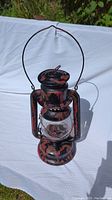 Front view of the antique red Beacon oil lamp showing handle, top ventilation, and the distressed red and black paint