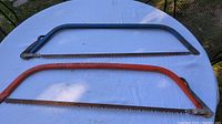 Two bow hand saws lying on a white surface outdoors, showing overall size and shape.