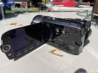 View of camcorder with LCD screen flipped out showing side control buttons and battery release area.