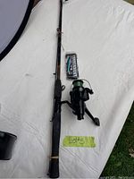 Full view of fishing rod with attached reel, and sealed lure pack placed next to rod on white surface.
