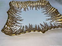 Top view showing square plate with scalloped edges and gold painted leaf and vine design around the rim