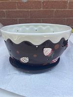 Side profile of ceramic bowl showing brown exterior with white wavy rim glaze and strawberry hole cutouts, plus matching drip plate beneath.