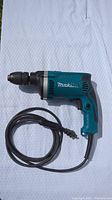 Side view of Makita hammer drill on white fabric background showing full tool length and cord.
