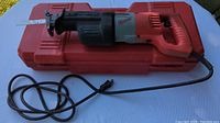 Side view of the Milwaukee heavy duty Sawzall with attached blade and power cord on red case.