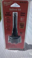 Front view of Milwaukee selfeed bit in original sealed packaging, clear blister plastic on red backing card. Markings include size 2 1/8 inch and 'Fast Cutting Clean Holes'.