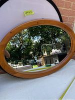 Front view of the oval pine wood framed mirror showing the reflective glass and the wood grain frame with some scuffs.