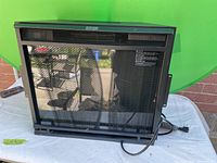 Front view of black metal electric firebox with mesh front and glass display, plugged in with a visible power cord.