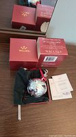 Photo showing the 2010 Wallace 40th Anniversary Bell ornament inside its black velvet pouch with the red Wallace box in the background along with paperwork.