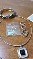 Photo showing silver snake chain necklace with black square pendant, silver hoop earrings, small square stud earrings, and snake pattern enamel bangle bracelet