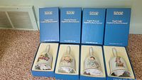 Four vintage Christmas bells with white handles, displayed in original blue Schmid boxes. Each bell shows a unique angel or child figure inspired by Berta Hummel's works.