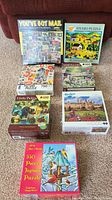 Seven assorted boxed jigsaw puzzles arranged on carpet showing variety of puzzle artwork and boxes