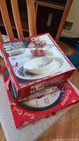 Stack showing Lenox Holiday children's dishware in original packaging on top of a Christmas Carol clock box.