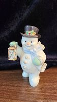 Front view of the Lenox ceramic snowman holding a lantern in right hand and a sack in left arm, detailed with metallic accents on hat, buttons, and lantern.