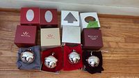 Top-down photo showing all 4 silver-plated Wallace sleigh bell ornaments displayed in their original soft pouches with their branded boxes behind them on wooden floor.