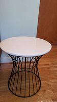 Front view showing the round white plastic top and black wire base in a flared hourglass shape.