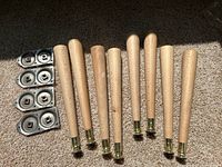 Set of eight tapered wooden furniture legs with brass caps laid out on carpet, with four metal mounting plates to attach to furniture.