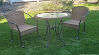 Full view of the patio table and two wicker chairs on grass.