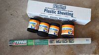 Shot displaying FilmGard branded plastic sheeting box along with rolls of Frost King gutter guard and Typar landscape fabric roll.