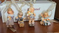 Four Studio Hummel children's figurine ornaments with hanging ribbons and original box in background